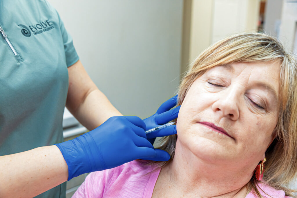 A woman turns her head and shuts her eyes as she receives Botox for TMJ in Craven County.