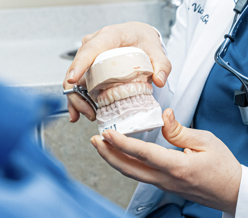 A provider in a white lab coat holds a set of fake teeth and explains the benefits of dentures in Craven County.
