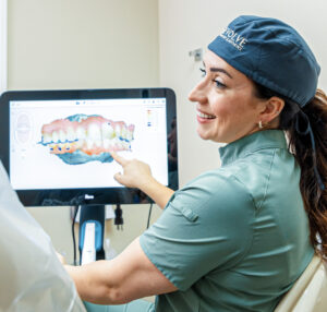 A provider in scrubs smiles and points at a screen showing a scan of teeth for Invisalign in Craven County.
