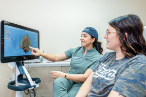 A provider in scrubs laughs with a patient while she points at a screen outlining the process for Invisalign in Craven County.